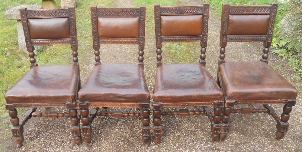 A set of four antique dark oak dining chairs featuring carved backrests, turned legs, and brown leather upholstered seats. View IV