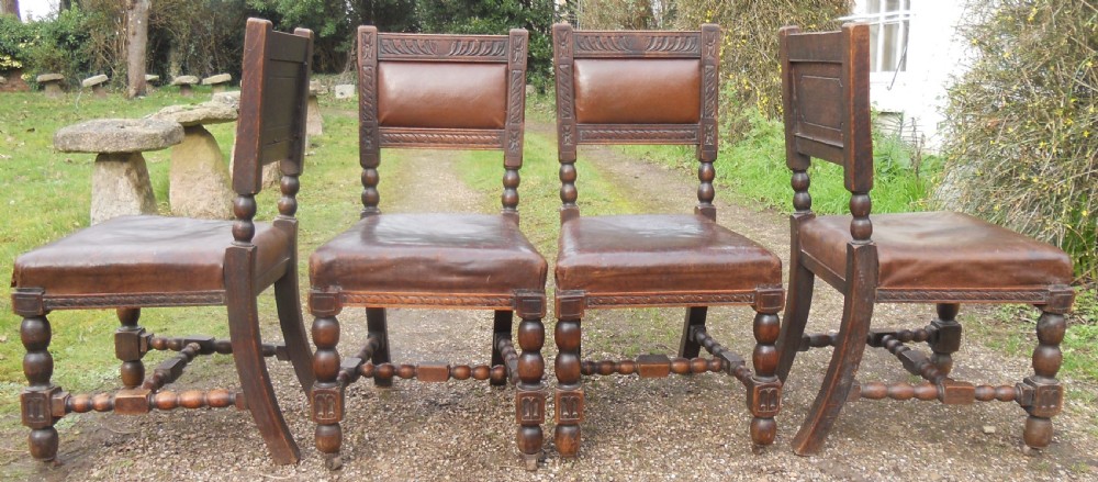 A set of four antique dark oak dining chairs featuring carved backrests, turned legs, and brown leather upholstered seats. View V