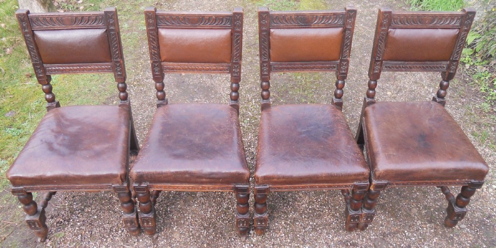 A set of four antique dark oak dining chairs featuring carved backrests, turned legs, and brown leather upholstered seats. View VI