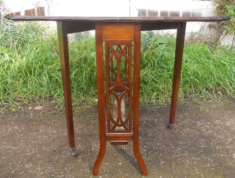 An Edwardian mahogany drop-leaf occasional table featuring scalloped edges, a lower stretcher shelf, and slender legs on brass castors. View V