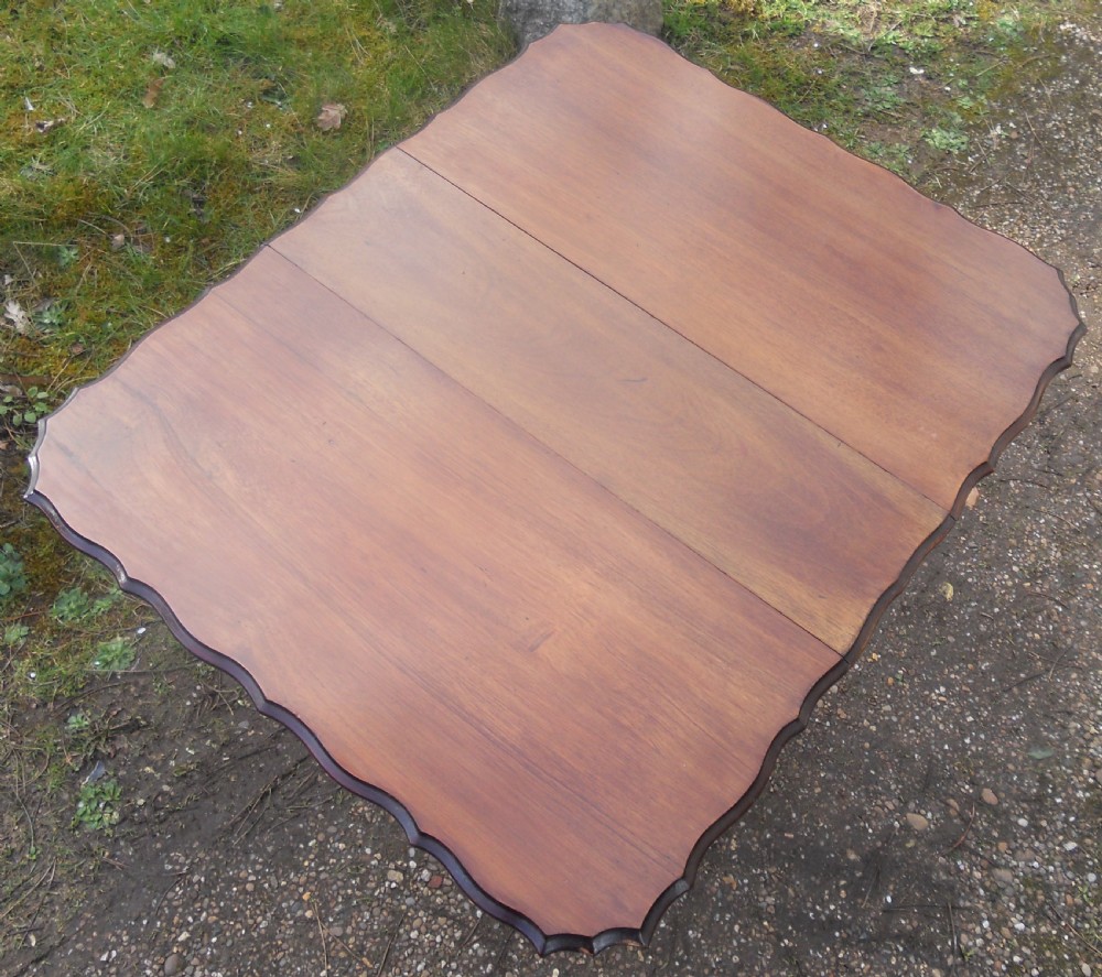 An Edwardian mahogany drop-leaf occasional table featuring scalloped edges, a lower stretcher shelf, and slender legs on brass castors. View VII