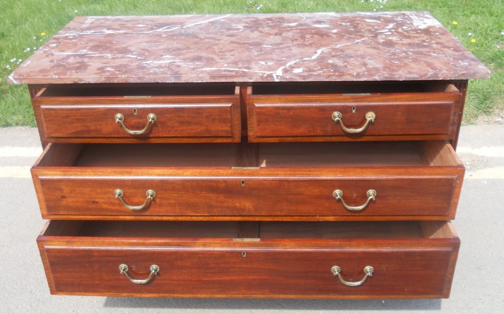 An Edwardian mahogany chest of drawers featuring a variegated red marble top, brass drop handles, and tapered legs on castors. View VII