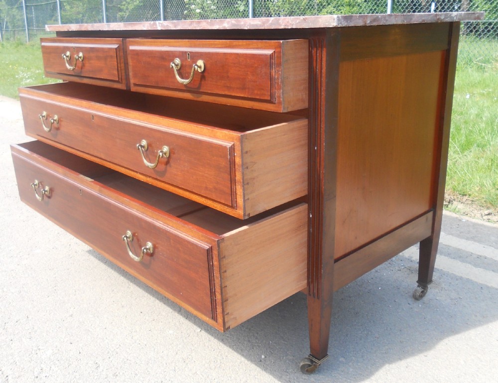 An Edwardian mahogany chest of drawers featuring a variegated red marble top, brass drop handles, and tapered legs on castors. View VIII