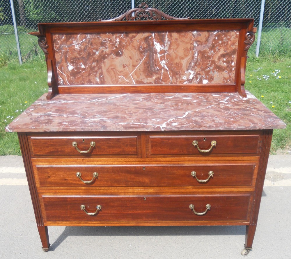 An Edwardian mahogany chest of drawers featuring a variegated red marble top, brass drop handles, and tapered legs on castors. View XII