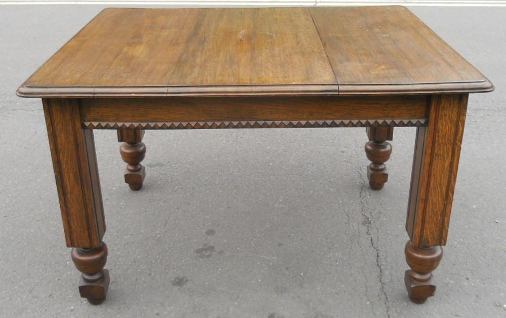 A rectangular Edwardian solid oak dining table featuring turned legs and a carved geometric frieze along the apron.