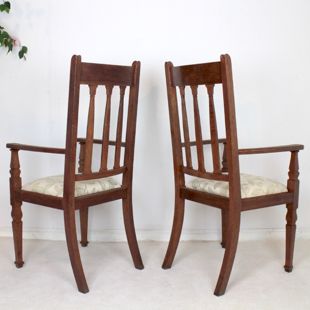 A pair of medium brown oak Arts and Crafts armchairs with carved circular back details, vertical splats, turned front legs, and light-coloured patterned seat cushions. View V