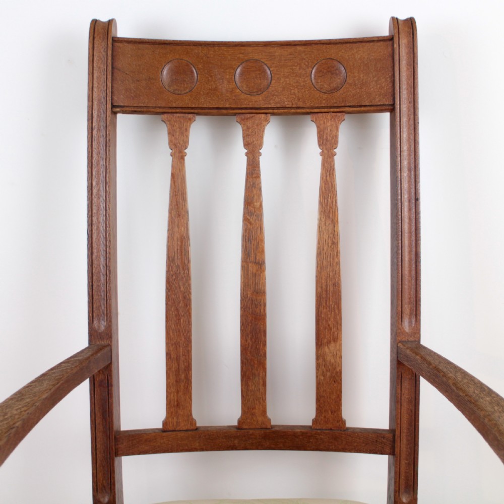 A pair of medium brown oak Arts and Crafts armchairs with carved circular back details, vertical splats, turned front legs, and light-coloured patterned seat cushions. View VIII