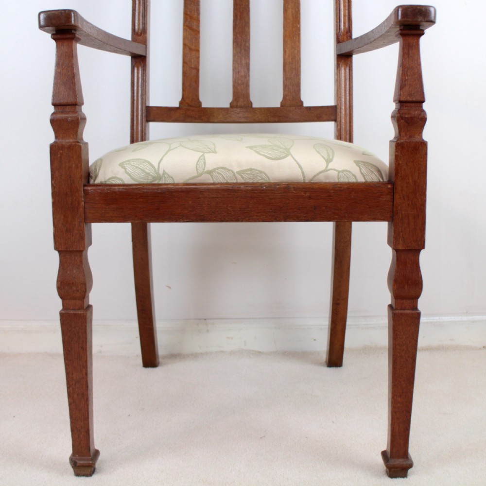 A pair of medium brown oak Arts and Crafts armchairs with carved circular back details, vertical splats, turned front legs, and light-coloured patterned seat cushions. View IX