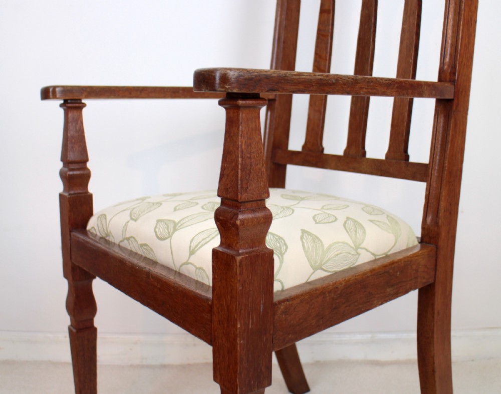 A pair of medium brown oak Arts and Crafts armchairs with carved circular back details, vertical splats, turned front legs, and light-coloured patterned seat cushions. View X