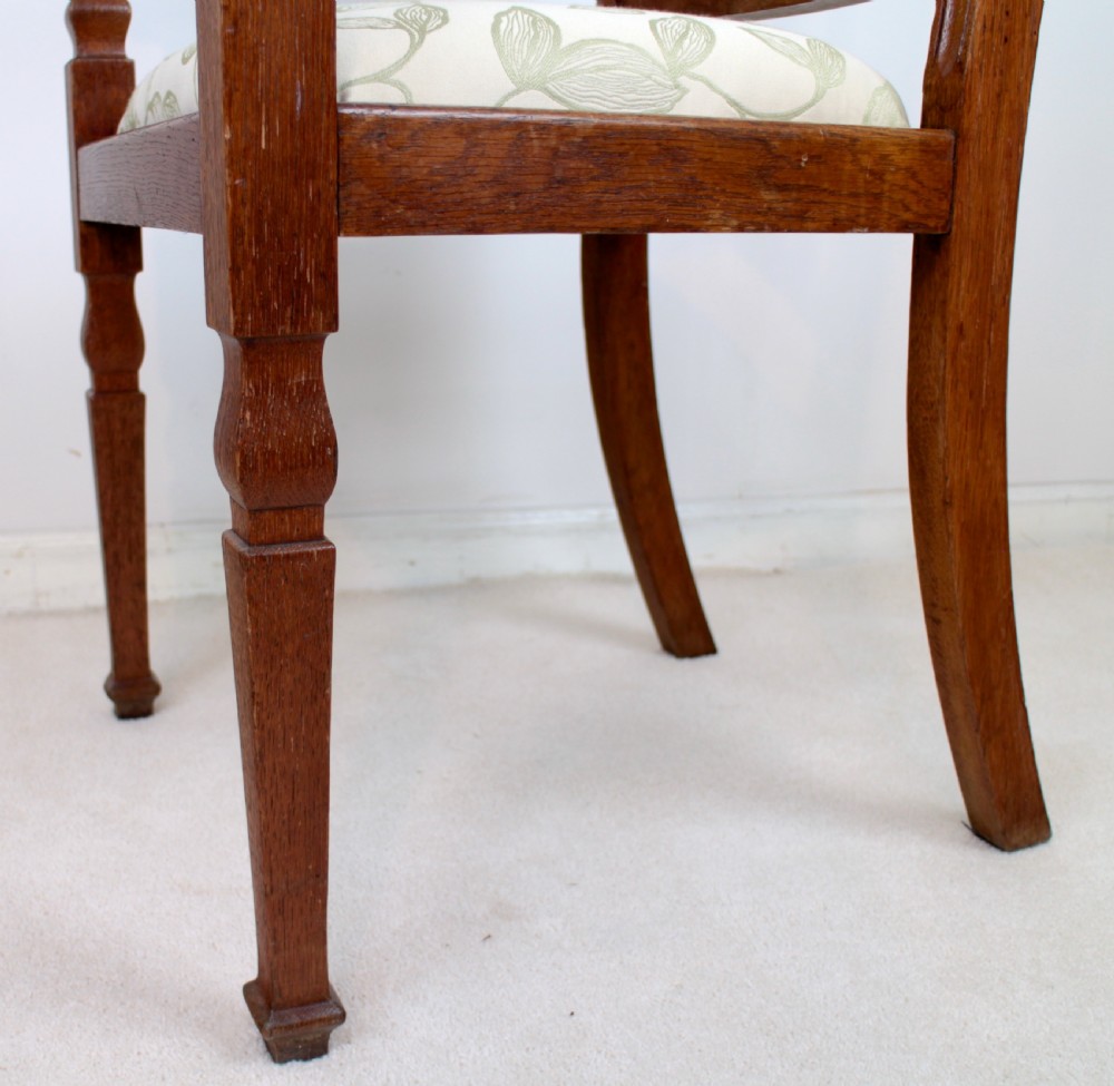 A pair of medium brown oak Arts and Crafts armchairs with carved circular back details, vertical splats, turned front legs, and light-coloured patterned seat cushions. View XI