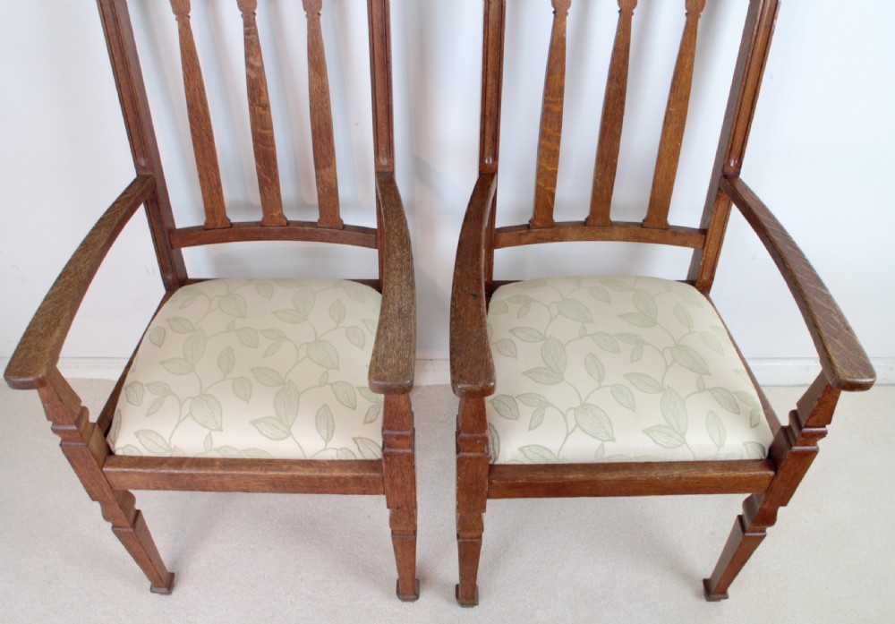 A pair of medium brown oak Arts and Crafts armchairs with carved circular back details, vertical splats, turned front legs, and light-coloured patterned seat cushions. View XII