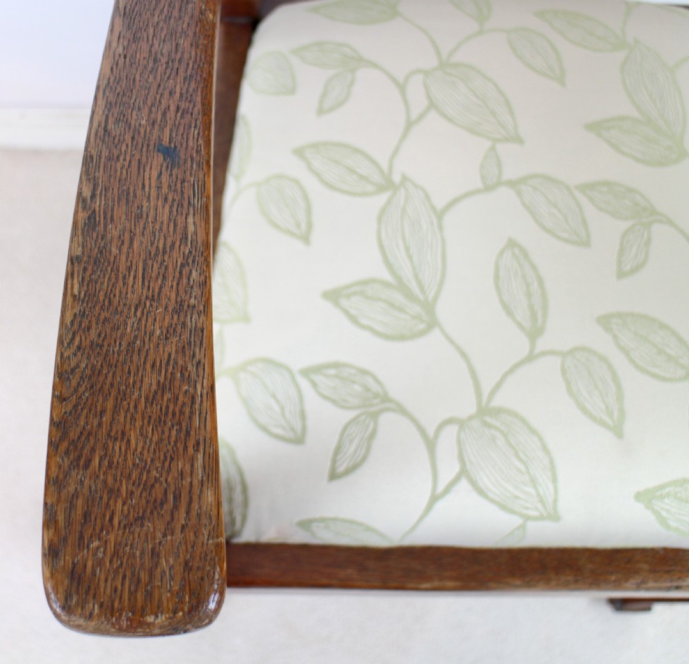 A pair of medium brown oak Arts and Crafts armchairs with carved circular back details, vertical splats, turned front legs, and light-coloured patterned seat cushions. View XIII