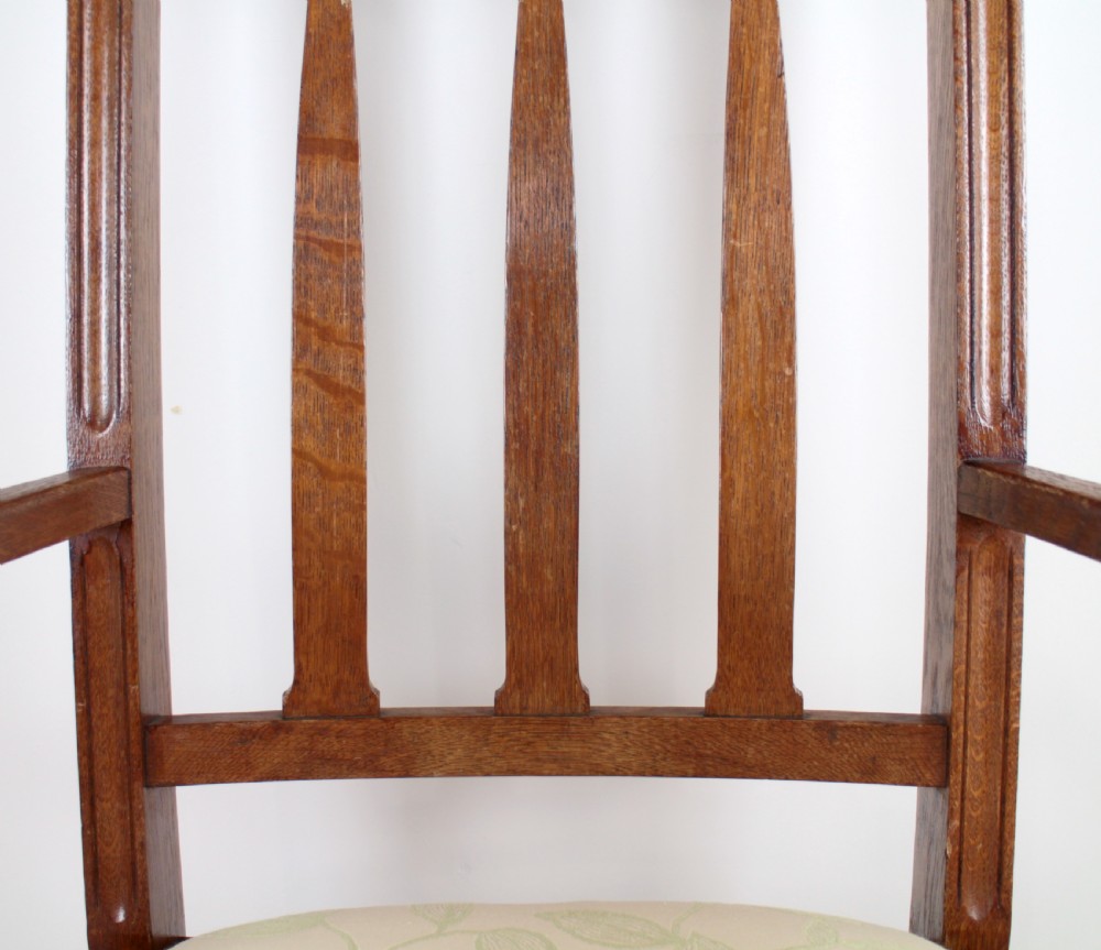 A pair of medium brown oak Arts and Crafts armchairs with carved circular back details, vertical splats, turned front legs, and light-coloured patterned seat cushions. View XVI