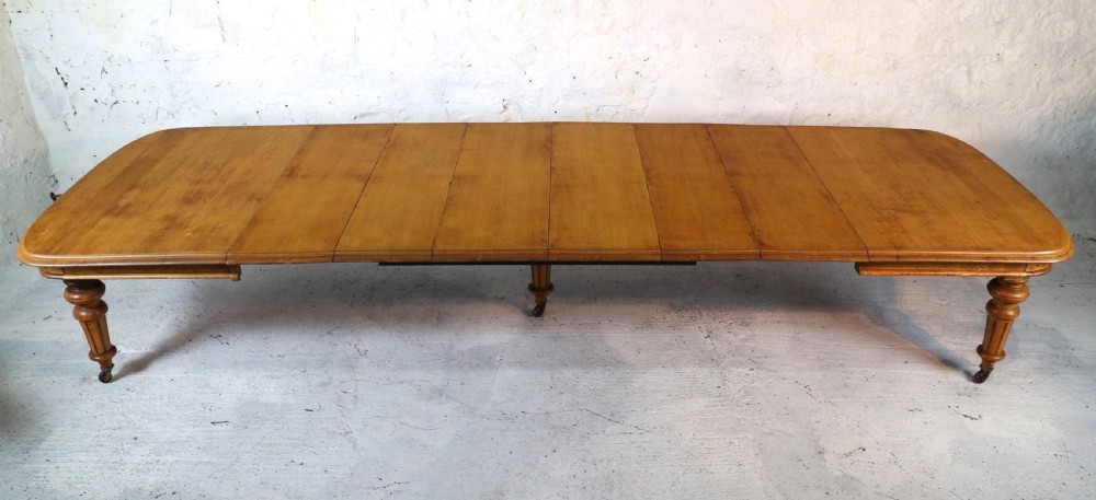 An extended early Victorian oak dining table featuring turned fluted legs set on brass castors with rounded corners and removable insert leaves. View II