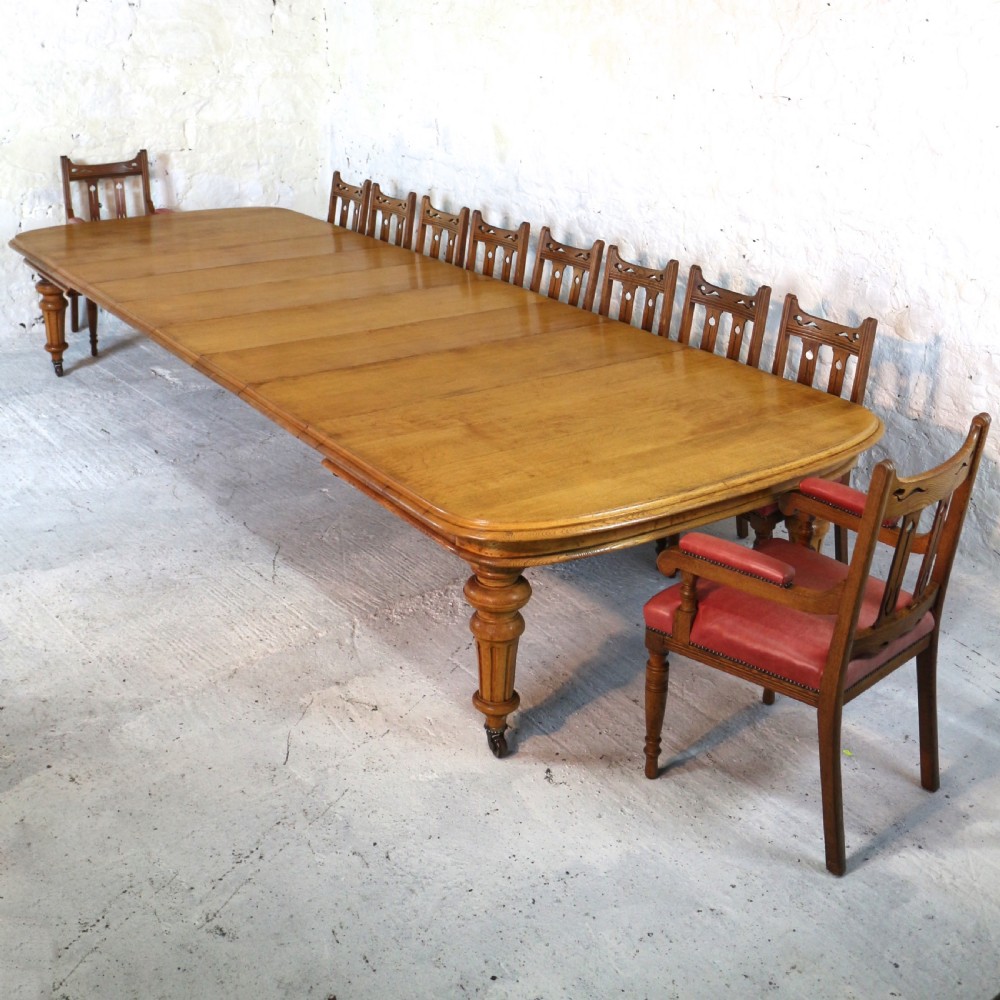 An extended early Victorian oak dining table featuring turned fluted legs set on brass castors with rounded corners and removable insert leaves. View III