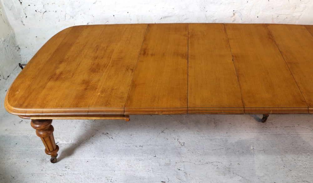 An extended early Victorian oak dining table featuring turned fluted legs set on brass castors with rounded corners and removable insert leaves. View IV