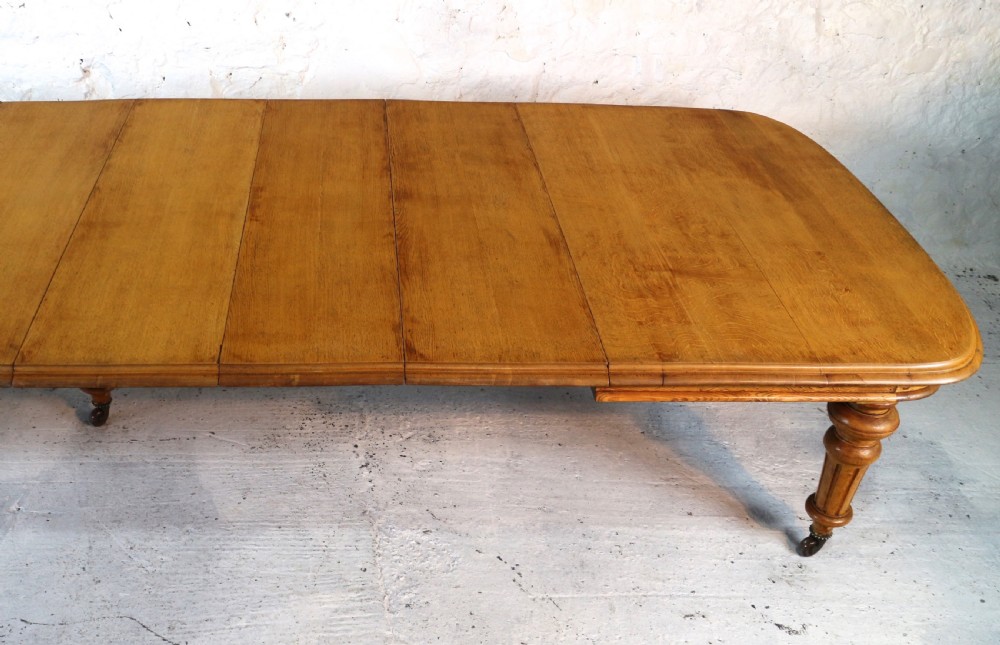 An extended early Victorian oak dining table featuring turned fluted legs set on brass castors with rounded corners and removable insert leaves. View V