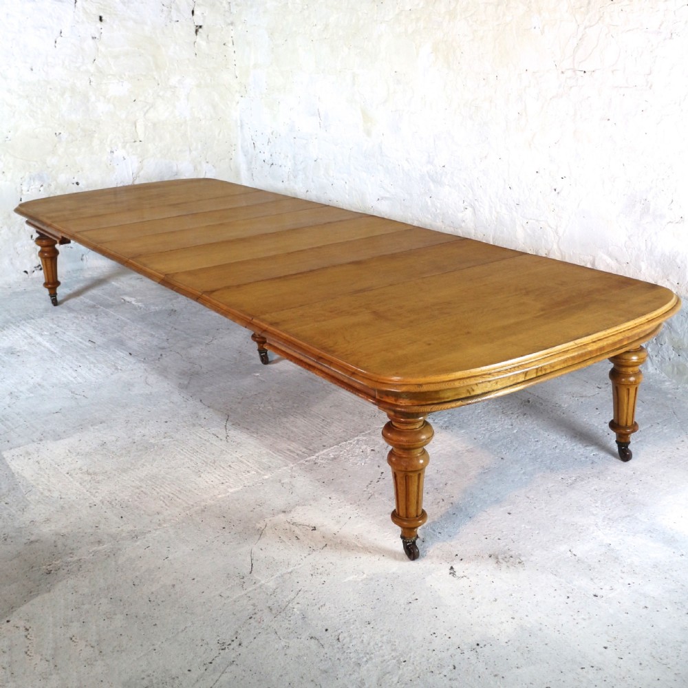 An extended early Victorian oak dining table featuring turned fluted legs set on brass castors with rounded corners and removable insert leaves. View VI