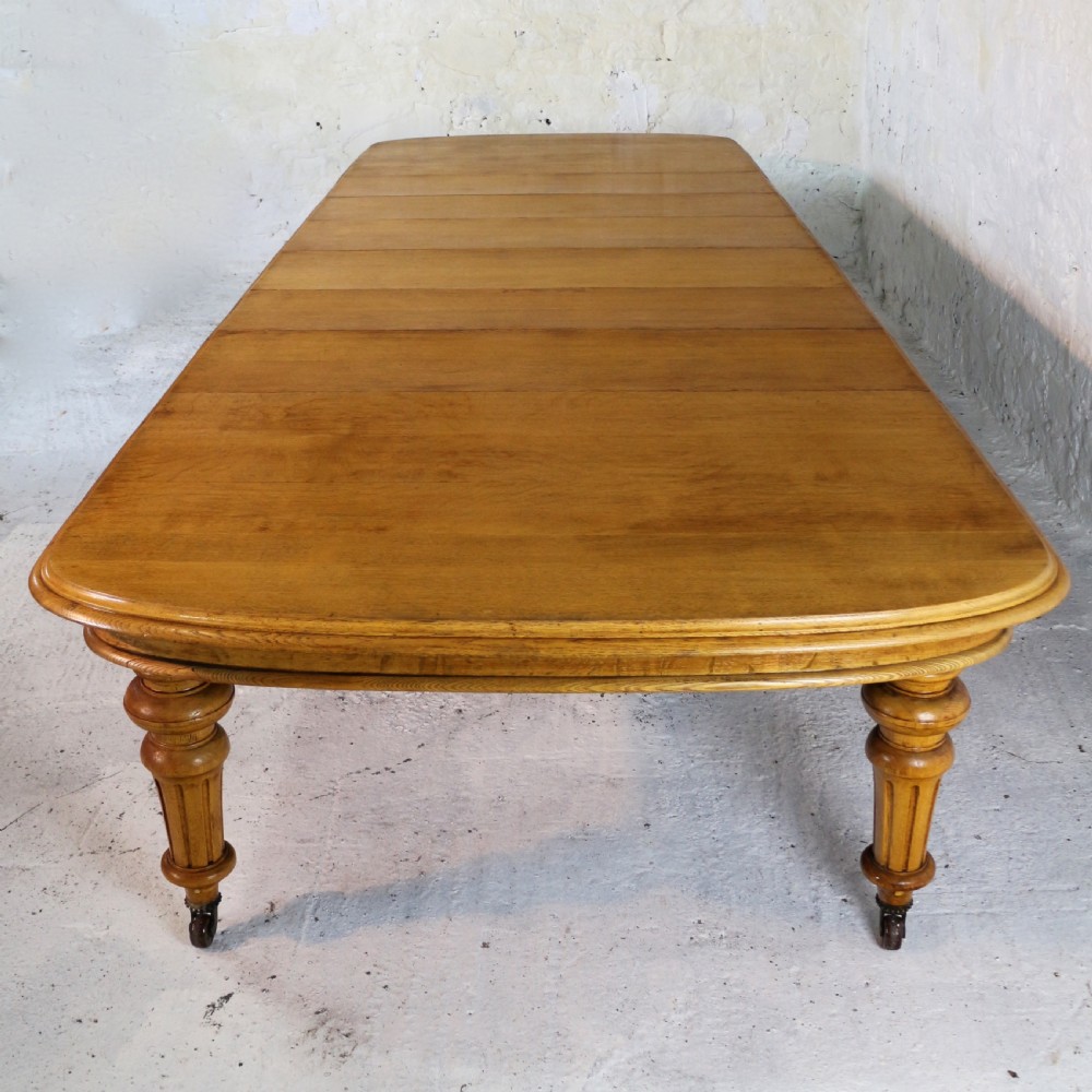 An extended early Victorian oak dining table featuring turned fluted legs set on brass castors with rounded corners and removable insert leaves. View VII
