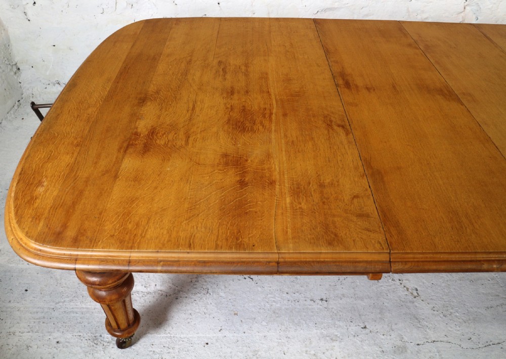An extended early Victorian oak dining table featuring turned fluted legs set on brass castors with rounded corners and removable insert leaves. View VIII