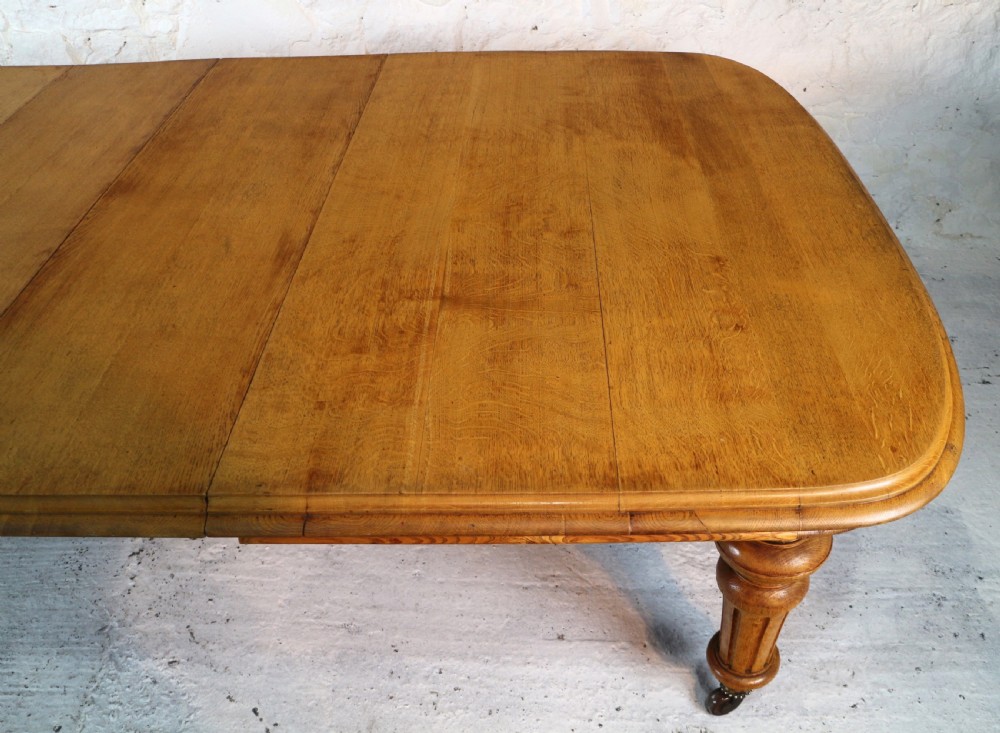An extended early Victorian oak dining table featuring turned fluted legs set on brass castors with rounded corners and removable insert leaves. View IX