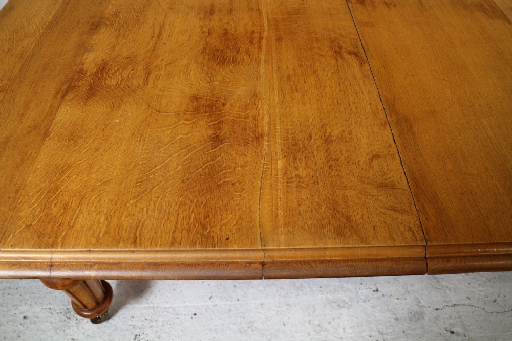 An extended early Victorian oak dining table featuring turned fluted legs set on brass castors with rounded corners and removable insert leaves. View XIII