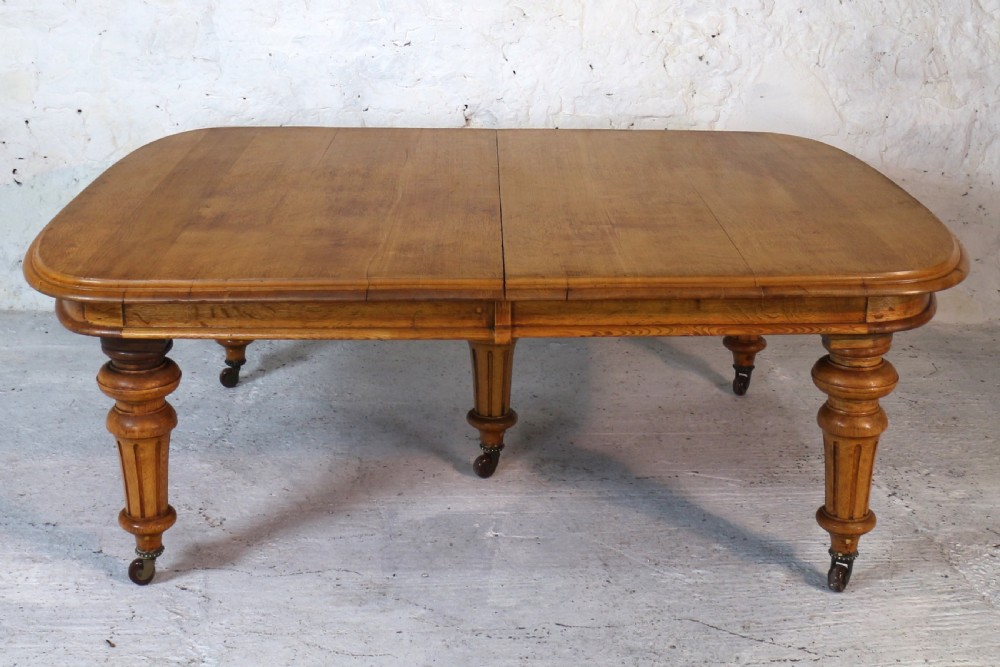 An extended early Victorian oak dining table featuring turned fluted legs set on brass castors with rounded corners and removable insert leaves. View XIV