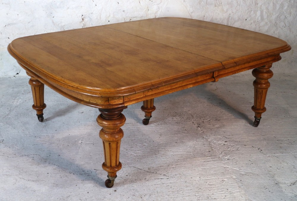 An extended early Victorian oak dining table featuring turned fluted legs set on brass castors with rounded corners and removable insert leaves. View XV