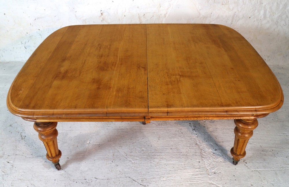 An extended early Victorian oak dining table featuring turned fluted legs set on brass castors with rounded corners and removable insert leaves. View XVI