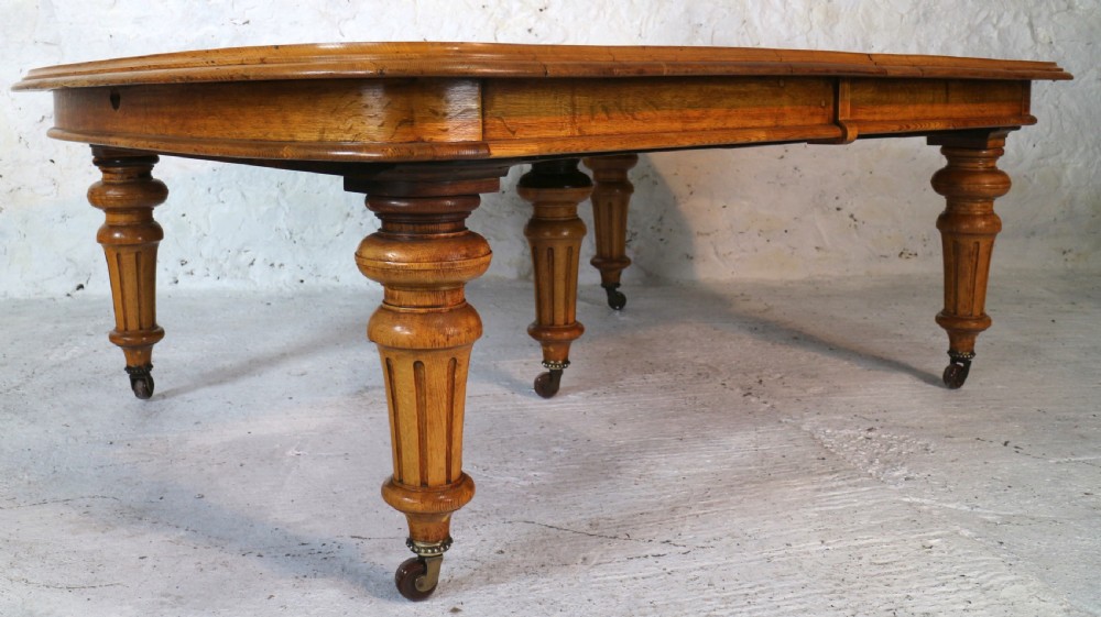 An extended early Victorian oak dining table featuring turned fluted legs set on brass castors with rounded corners and removable insert leaves. View XVII