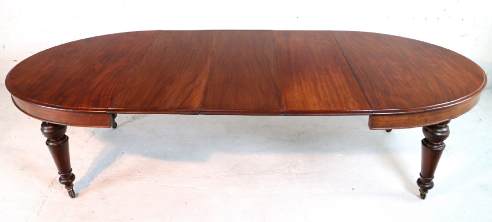 An extended Victorian Cuban mahogany dining table with rounded ends, turned legs, and brass castors. View V