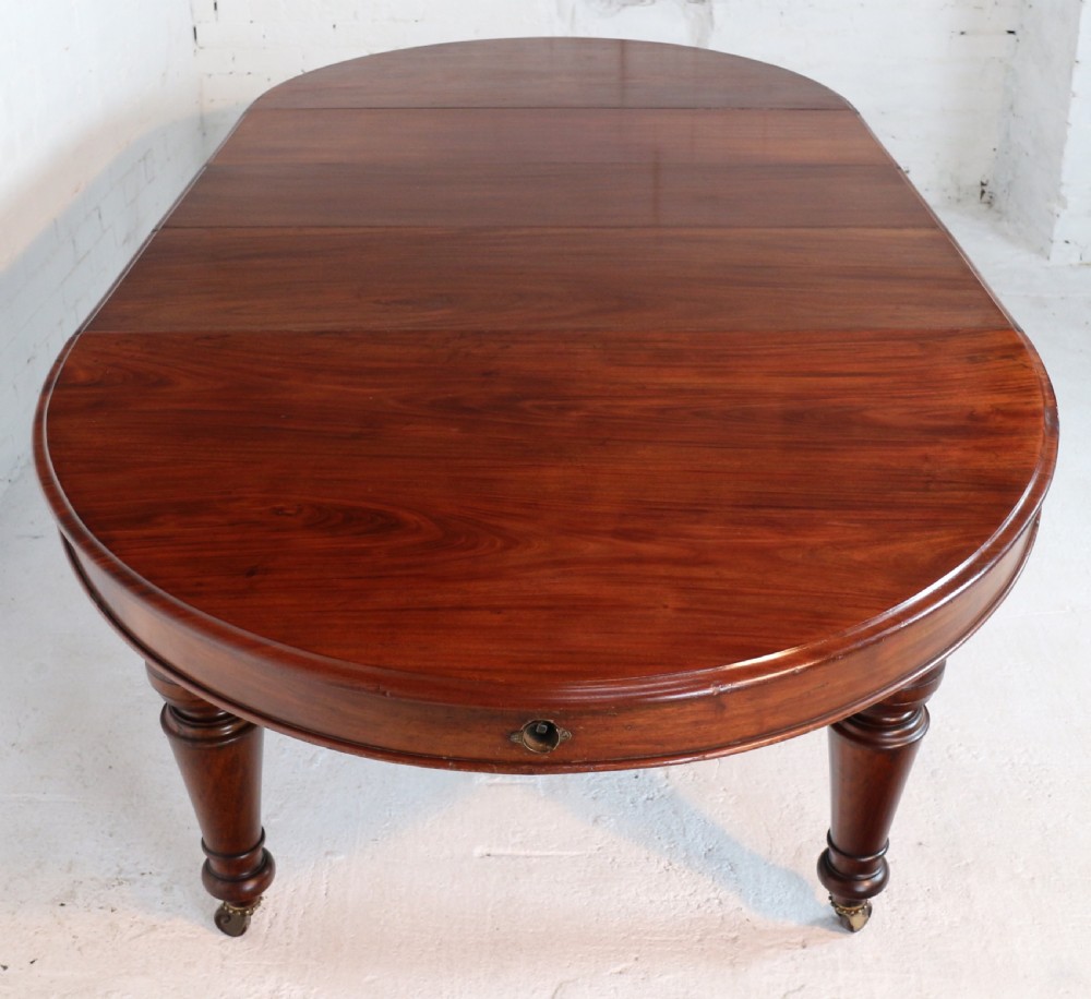 An extended Victorian Cuban mahogany dining table with rounded ends, turned legs, and brass castors. View VI