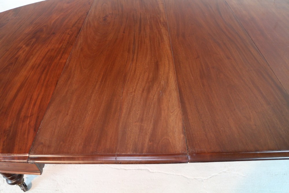 An extended Victorian Cuban mahogany dining table with rounded ends, turned legs, and brass castors. View XV