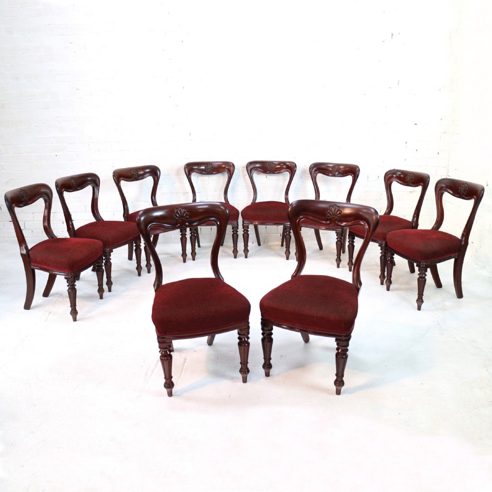 A set of ten William IV mahogany dining chairs with carved top rails, turned front legs, and deep red upholstery.