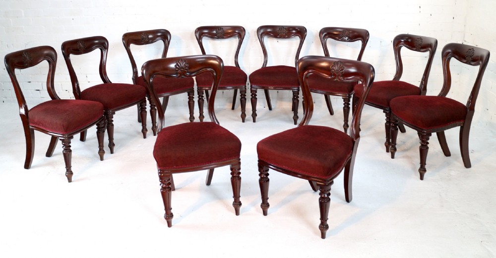 A set of ten William IV mahogany dining chairs with carved top rails, turned front legs, and deep red upholstery. View II