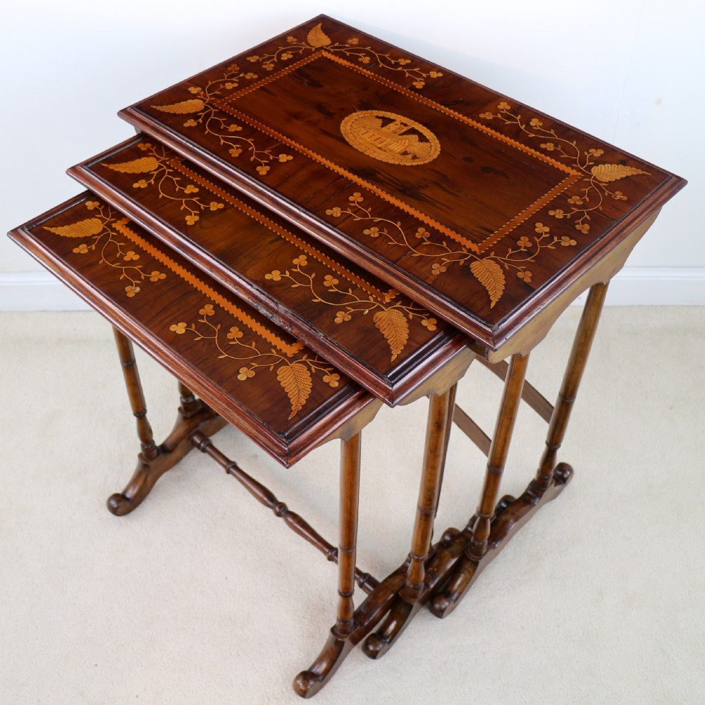 A set of three nested wooden side tables featuring detailed marquetry inlays of foliage and central vignettes, supported by slender turned legs and scroll feet. View IX