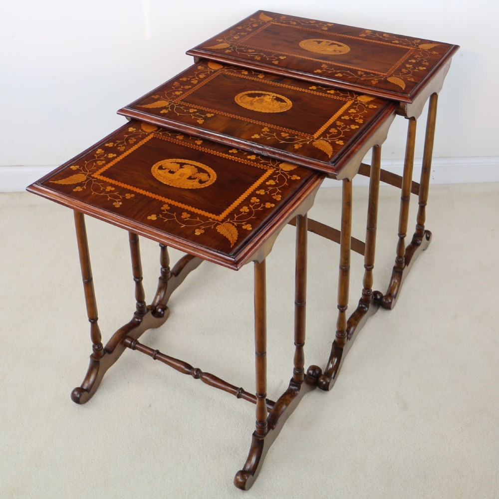 A set of three nested wooden side tables featuring detailed marquetry inlays of foliage and central vignettes, supported by slender turned legs and scroll feet. View X