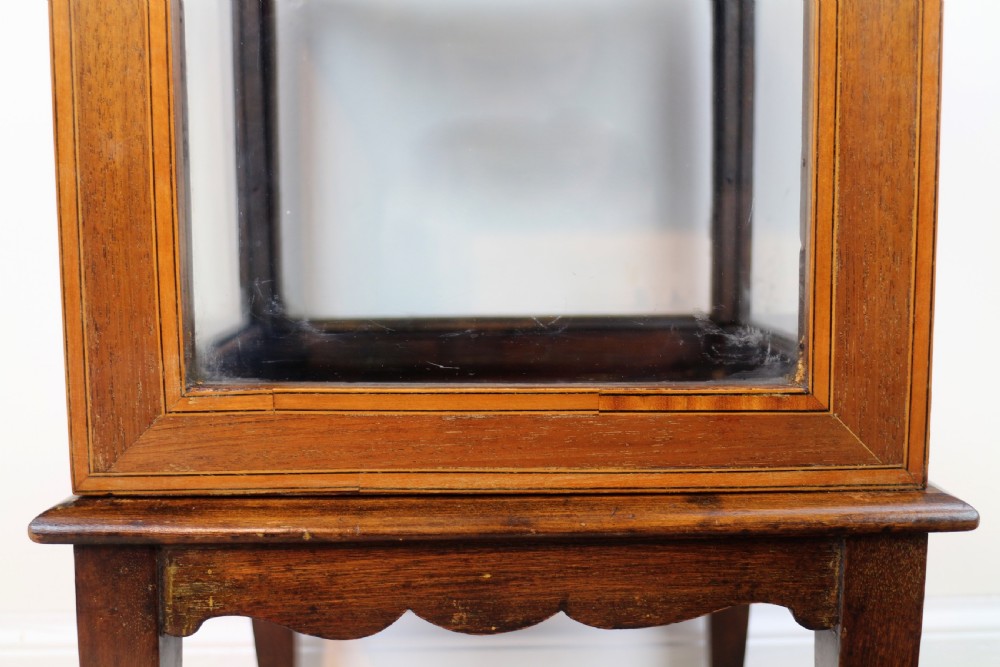A tall Edwardian mahogany glazed bijouterie cabinet featuring glass panels on all sides, two interior shelves, square tapered legs, and satinwood crossbanding. View XII