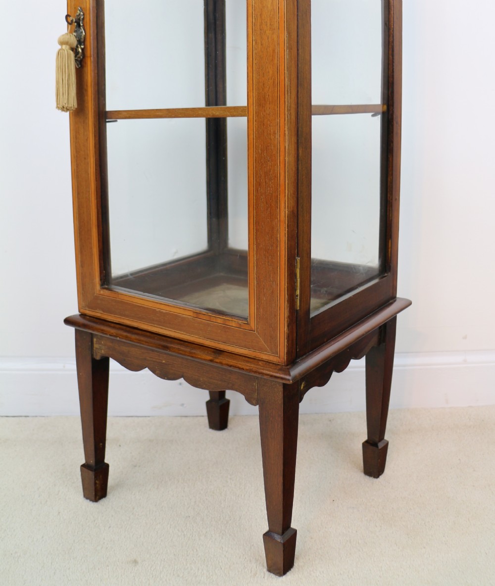 A tall Edwardian mahogany glazed bijouterie cabinet featuring glass panels on all sides, two interior shelves, square tapered legs, and satinwood crossbanding. View XIII