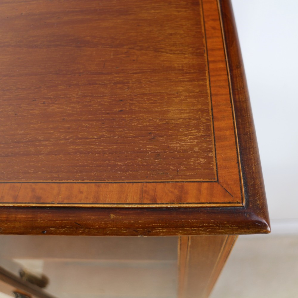 A tall Edwardian mahogany glazed bijouterie cabinet featuring glass panels on all sides, two interior shelves, square tapered legs, and satinwood crossbanding. View XV