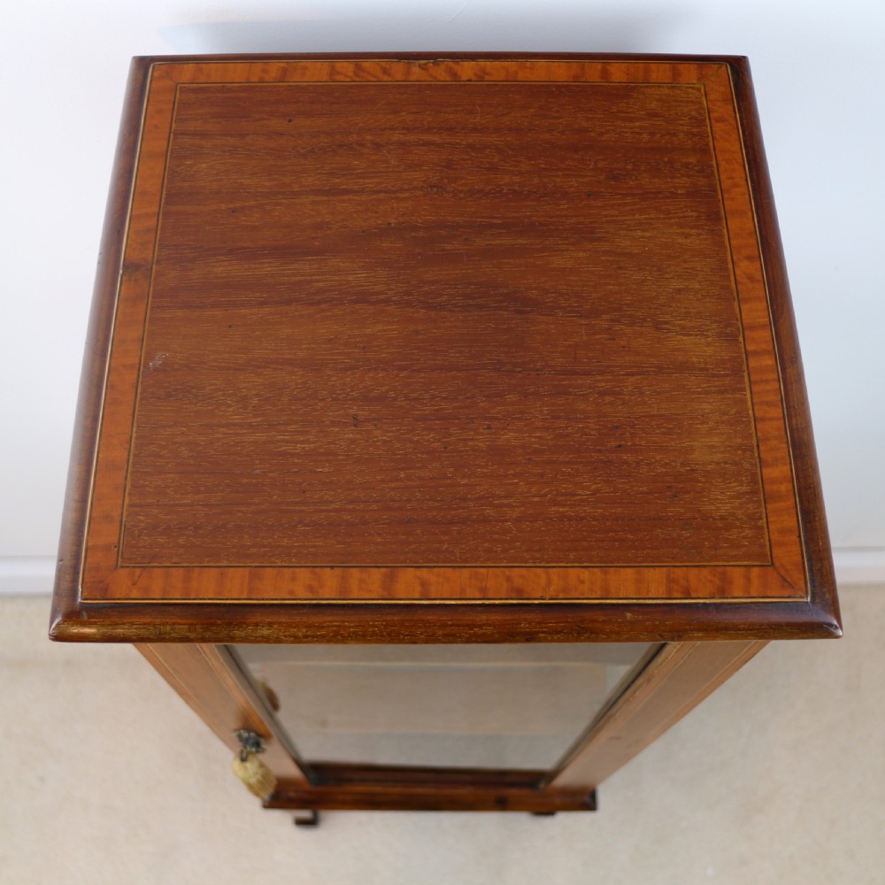 A tall Edwardian mahogany glazed bijouterie cabinet featuring glass panels on all sides, two interior shelves, square tapered legs, and satinwood crossbanding. View XVII