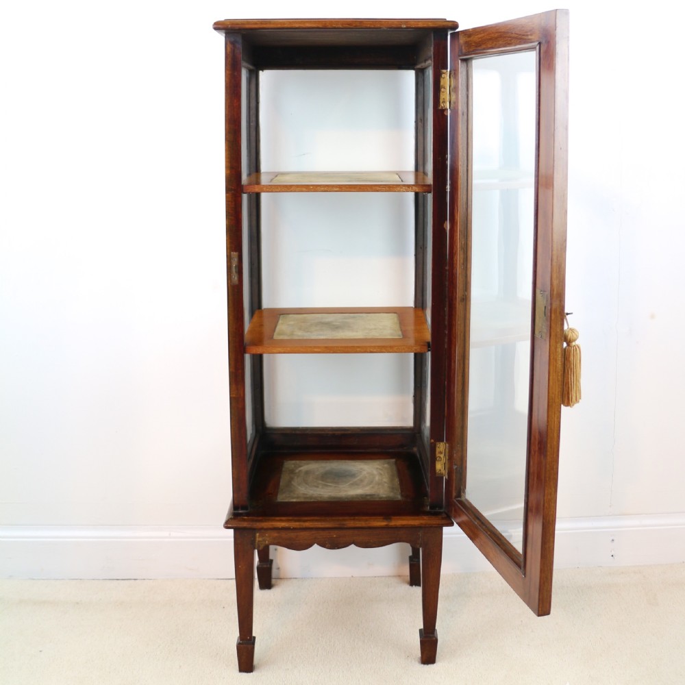 A tall Edwardian mahogany glazed bijouterie cabinet featuring glass panels on all sides, two interior shelves, square tapered legs, and satinwood crossbanding. View XIX