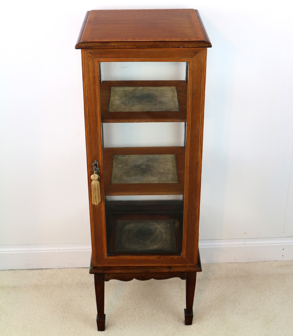 A tall Edwardian mahogany glazed bijouterie cabinet featuring glass panels on all sides, two interior shelves, square tapered legs, and satinwood crossbanding. View XX