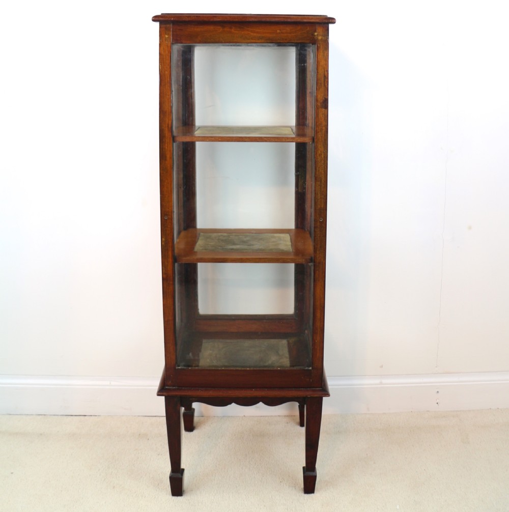 A tall Edwardian mahogany glazed bijouterie cabinet featuring glass panels on all sides, two interior shelves, square tapered legs, and satinwood crossbanding. View XXIV