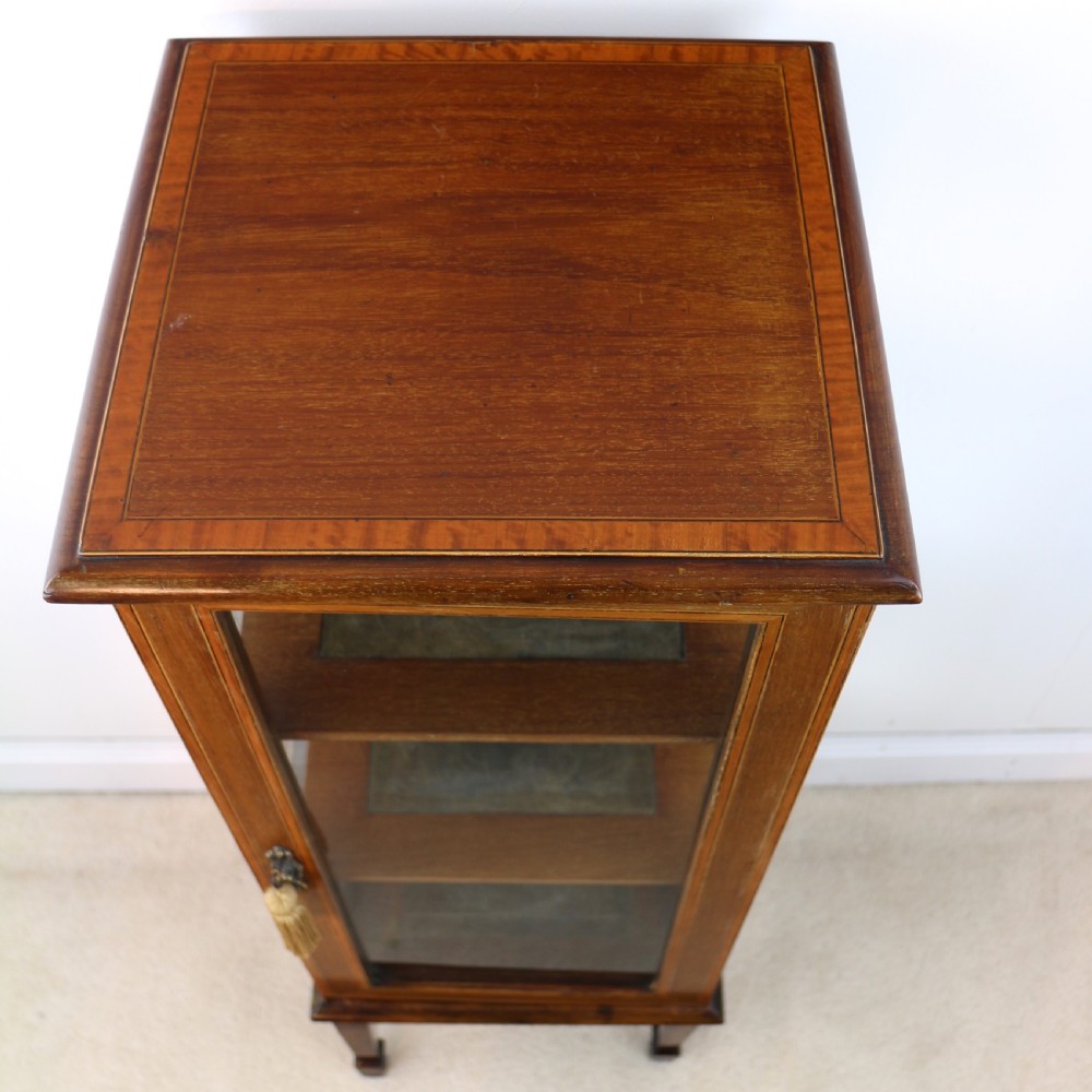 A tall Edwardian mahogany glazed bijouterie cabinet featuring glass panels on all sides, two interior shelves, square tapered legs, and satinwood crossbanding. View XXV