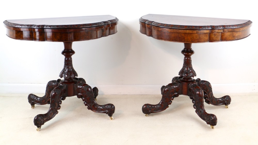 A pair of Victorian burr walnut fold-over card tables featuring shaped demi-lune tops, carved aprons, central turned pedestals, and carved quadform legs with castors. View II
