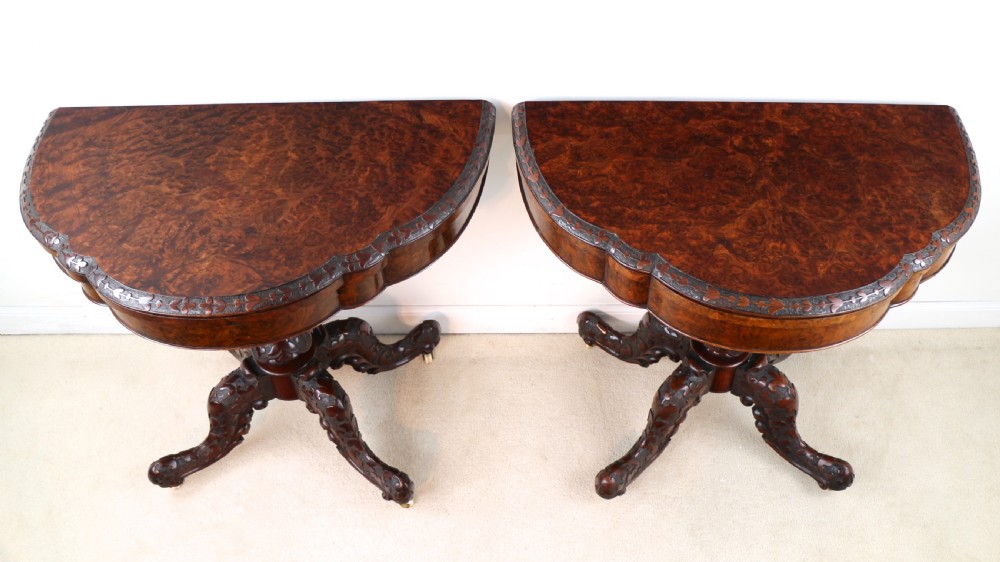 A pair of Victorian burr walnut fold-over card tables featuring shaped demi-lune tops, carved aprons, central turned pedestals, and carved quadform legs with castors. View VI