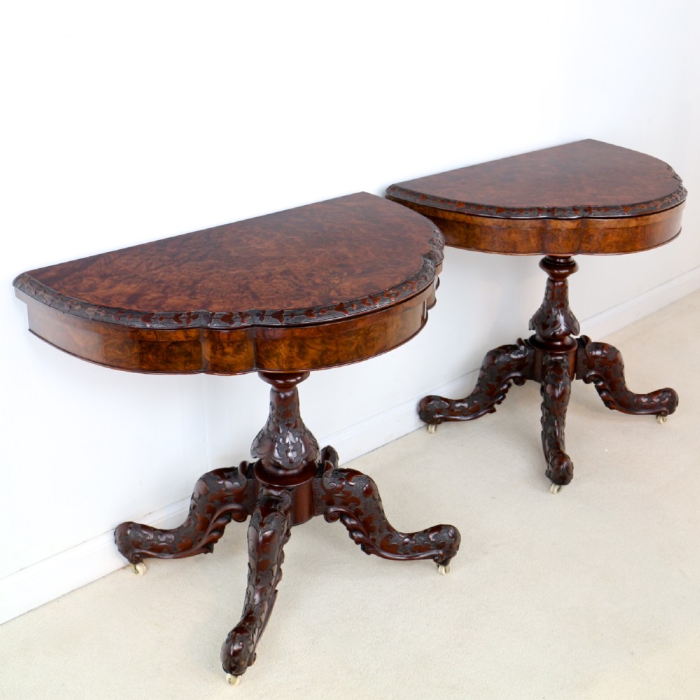 A pair of Victorian burr walnut fold-over card tables featuring shaped demi-lune tops, carved aprons, central turned pedestals, and carved quadform legs with castors. View VII