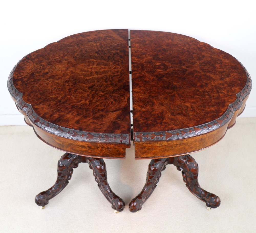 A pair of Victorian burr walnut fold-over card tables featuring shaped demi-lune tops, carved aprons, central turned pedestals, and carved quadform legs with castors. View X