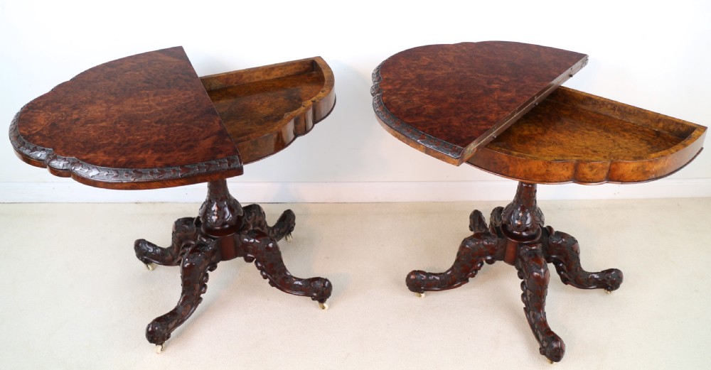 A pair of Victorian burr walnut fold-over card tables featuring shaped demi-lune tops, carved aprons, central turned pedestals, and carved quadform legs with castors. View XVI